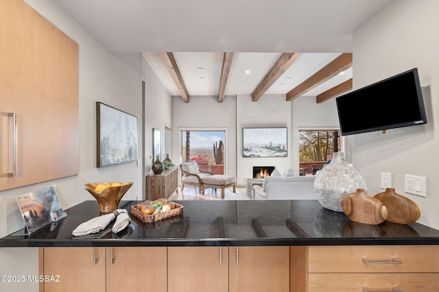 kitchen featuring a peninsula, a lit fireplace, beam ceiling, and light brown cabinetry