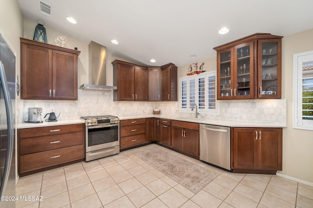 kitchen with appliances with stainless steel finishes, wall chimney range hood, decorative backsplash, sink, and light tile patterned floors