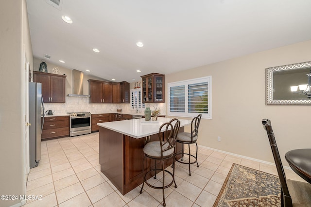 kitchen featuring lofted ceiling, backsplash, a breakfast bar area, stainless steel appliances, and wall chimney exhaust hood