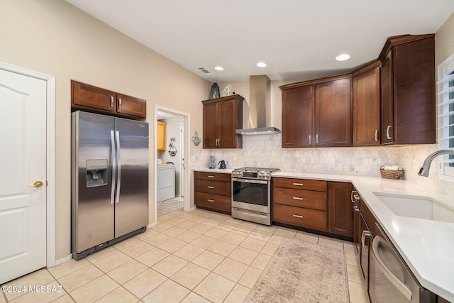 kitchen with wall chimney range hood, washer / clothes dryer, sink, appliances with stainless steel finishes, and light tile patterned floors