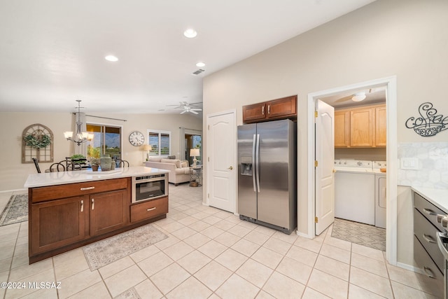 kitchen with vaulted ceiling, light tile patterned flooring, hanging light fixtures, separate washer and dryer, and stainless steel fridge