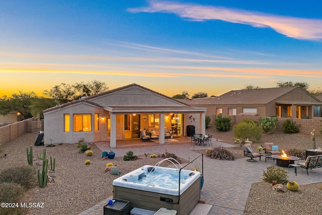 back house at dusk with a patio area, a hot tub, and a fire pit