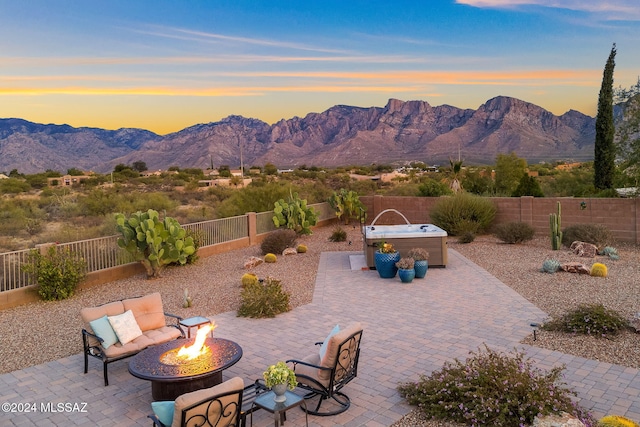 patio terrace at dusk with a mountain view, a hot tub, and an outdoor fire pit