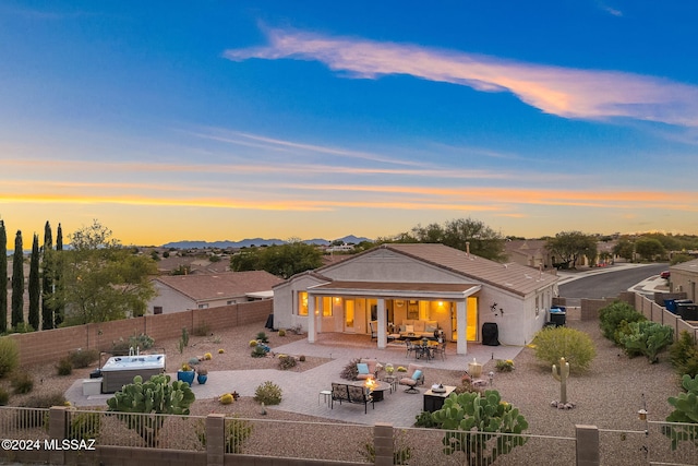 back house at dusk with an outdoor living space with a fire pit, a hot tub, and a patio