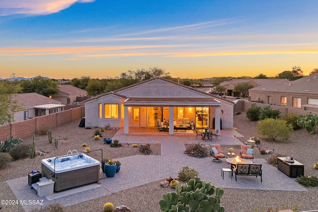 back house at dusk with a hot tub, a patio, and a fire pit