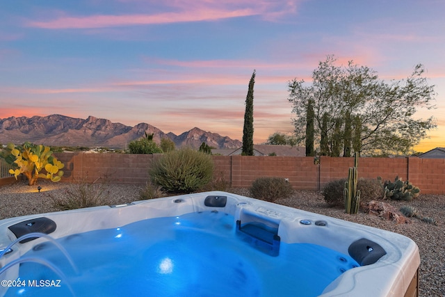 pool at dusk with a mountain view and a hot tub