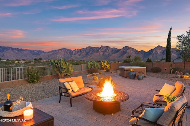 patio terrace at dusk with a mountain view, an outdoor fire pit, and a hot tub