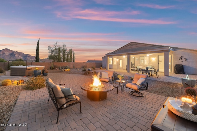 patio terrace at dusk featuring a mountain view, an outdoor fire pit, and a hot tub