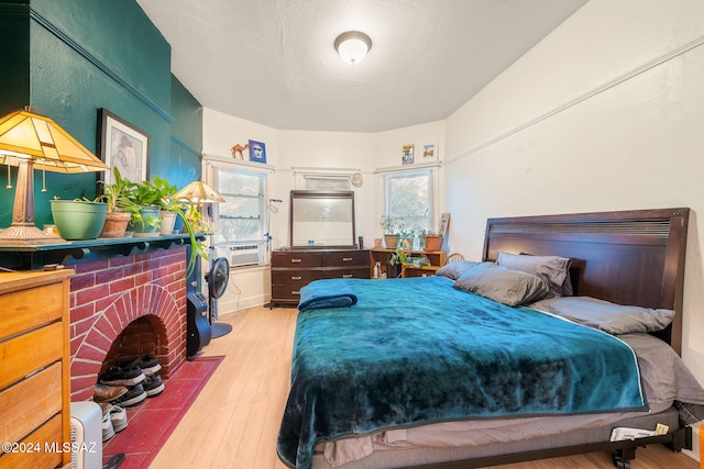 bedroom with multiple windows, hardwood / wood-style floors, and a brick fireplace