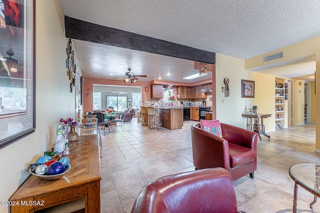 living room featuring ceiling fan, beam ceiling, light tile patterned floors, and a textured ceiling