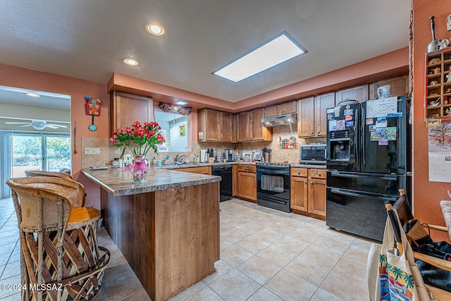 kitchen featuring tasteful backsplash, kitchen peninsula, light tile patterned flooring, and black appliances