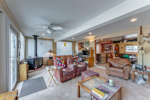 living room featuring ceiling fan, a wood stove, and light tile patterned floors