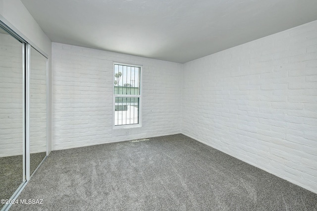 unfurnished bedroom featuring carpet flooring, a closet, and brick wall