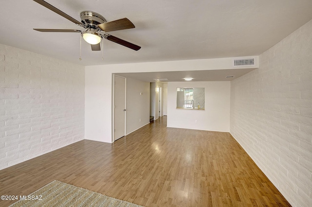 unfurnished room featuring ceiling fan, wood-type flooring, and brick wall