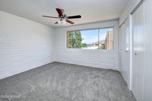 unfurnished bedroom with ceiling fan, carpet, brick wall, and two closets