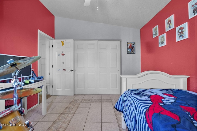 tiled bedroom with vaulted ceiling, a textured ceiling, ceiling fan, and a closet