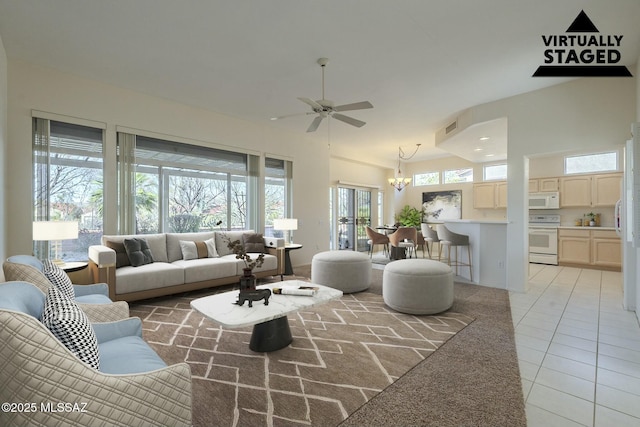 living area with light tile patterned floors, a high ceiling, ceiling fan with notable chandelier, and visible vents