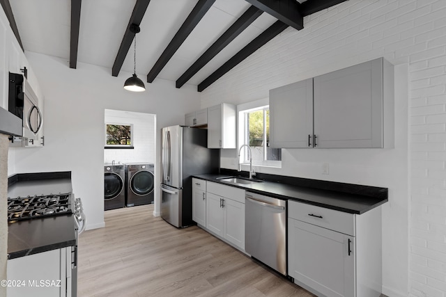 kitchen with appliances with stainless steel finishes, washer and clothes dryer, sink, pendant lighting, and light hardwood / wood-style floors