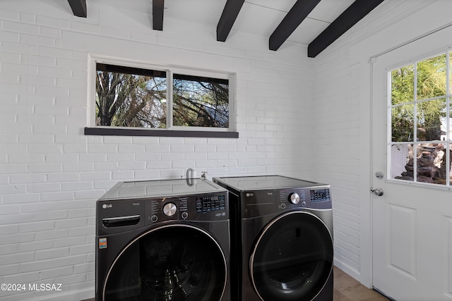 clothes washing area featuring washing machine and dryer and brick wall