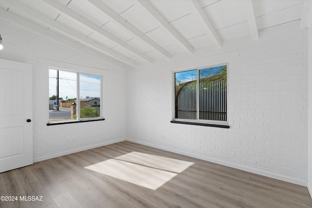 unfurnished room with hardwood / wood-style flooring, plenty of natural light, lofted ceiling with beams, and brick wall