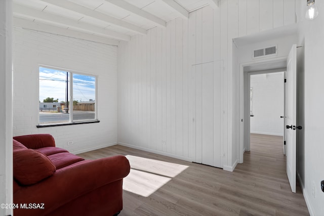 living area with beam ceiling, brick wall, and light wood-type flooring