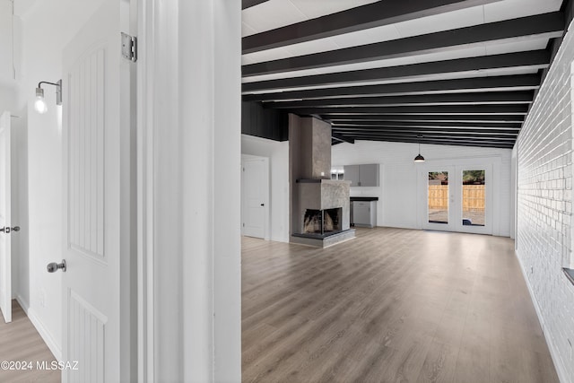 unfurnished living room featuring french doors, lofted ceiling with beams, light hardwood / wood-style flooring, a premium fireplace, and brick wall