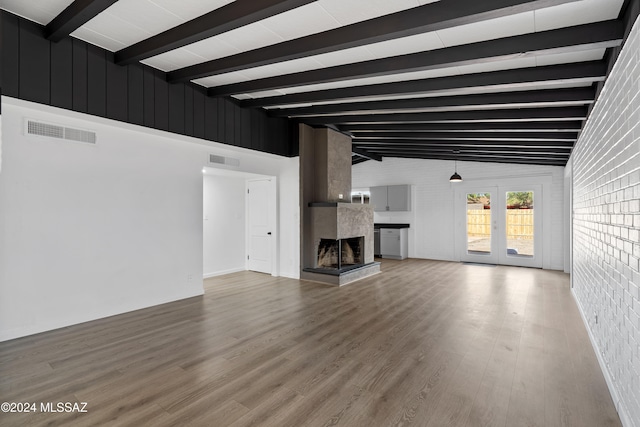 unfurnished living room featuring french doors, a large fireplace, lofted ceiling with beams, brick wall, and hardwood / wood-style flooring