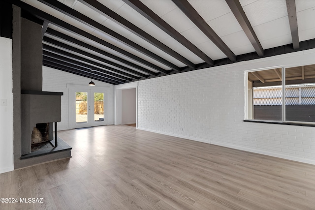 unfurnished living room with french doors, lofted ceiling with beams, light hardwood / wood-style flooring, and brick wall