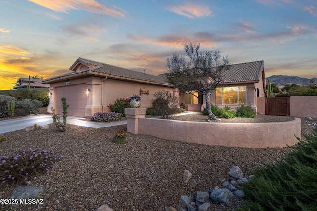 view of front of property featuring a tiled roof, concrete driveway, stucco siding, an attached garage, and a gate