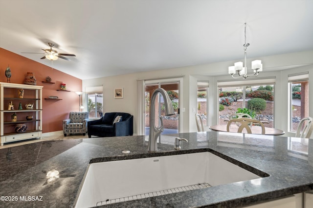 kitchen featuring lofted ceiling, dark stone counters, a sink, pendant lighting, and open floor plan