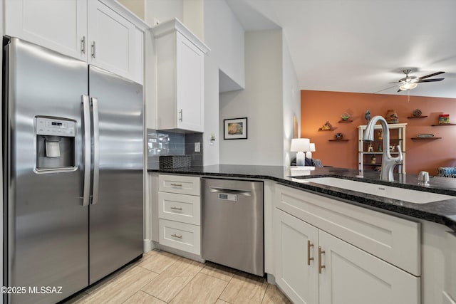 kitchen with a sink, backsplash, white cabinetry, stainless steel appliances, and dark stone counters