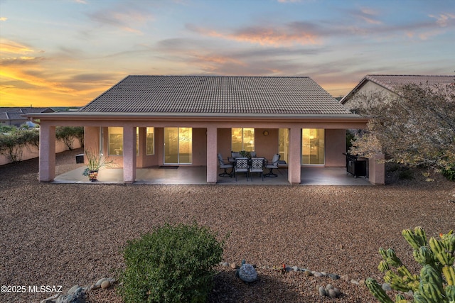 back of house at dusk featuring a patio area, stucco siding, and a tile roof