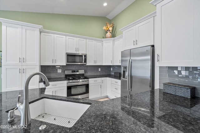 kitchen with a sink, white cabinetry, stainless steel appliances, dark stone counters, and decorative backsplash