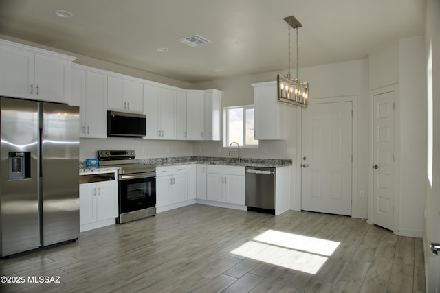 kitchen with decorative light fixtures, stainless steel appliances, and white cabinetry