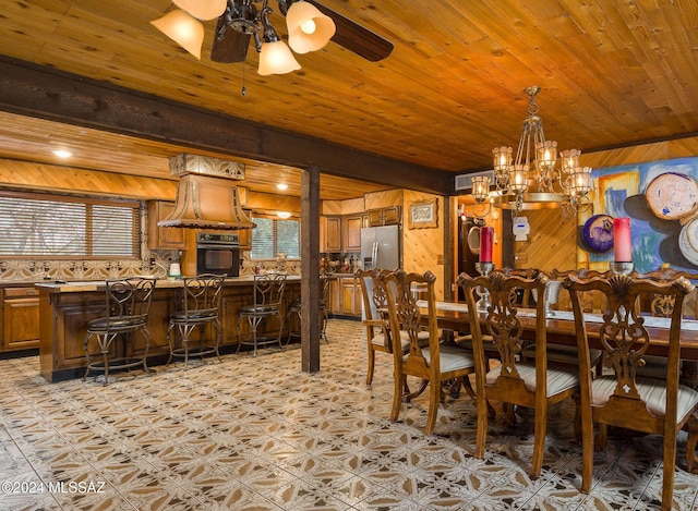 dining room with ceiling fan with notable chandelier, wood walls, and wooden ceiling