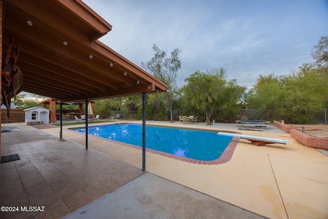 view of pool featuring a diving board, an outbuilding, and a patio