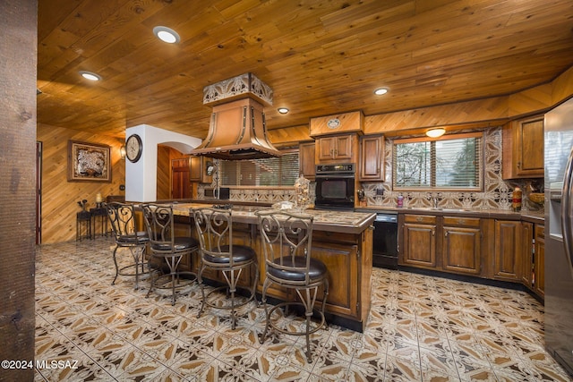 kitchen with a kitchen breakfast bar, wooden walls, decorative backsplash, a kitchen island, and black appliances