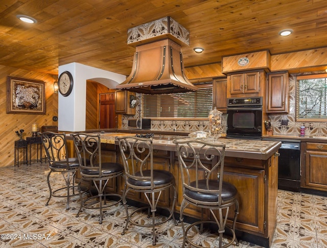 kitchen featuring a kitchen breakfast bar, island exhaust hood, wooden walls, a kitchen island, and black appliances