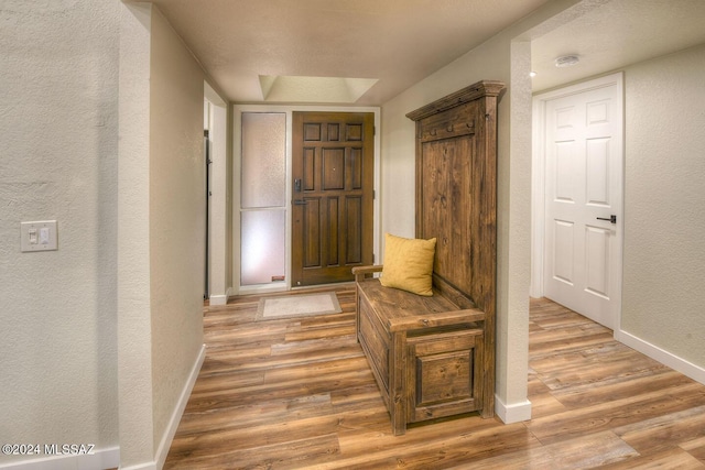 hall featuring light wood-style flooring, a textured wall, and baseboards