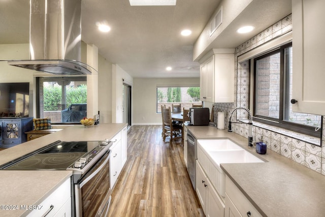 kitchen featuring wall chimney exhaust hood, appliances with stainless steel finishes, light wood-type flooring, and white cabinets