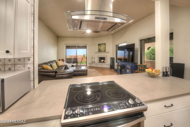 kitchen featuring extractor fan, open floor plan, a warm lit fireplace, electric stove, and white cabinetry