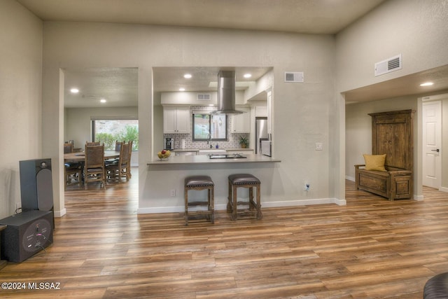 kitchen with visible vents, stainless steel fridge, island exhaust hood, and wood finished floors