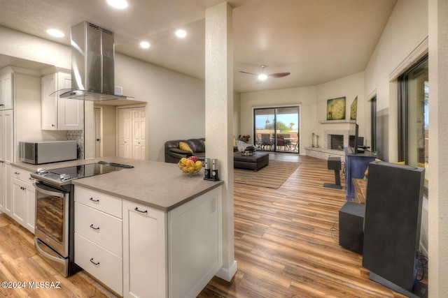 kitchen featuring white cabinetry, stainless steel range with electric cooktop, ceiling fan, wall chimney range hood, and light hardwood / wood-style flooring