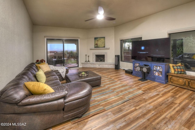 living room with a fireplace with raised hearth, a ceiling fan, and wood finished floors