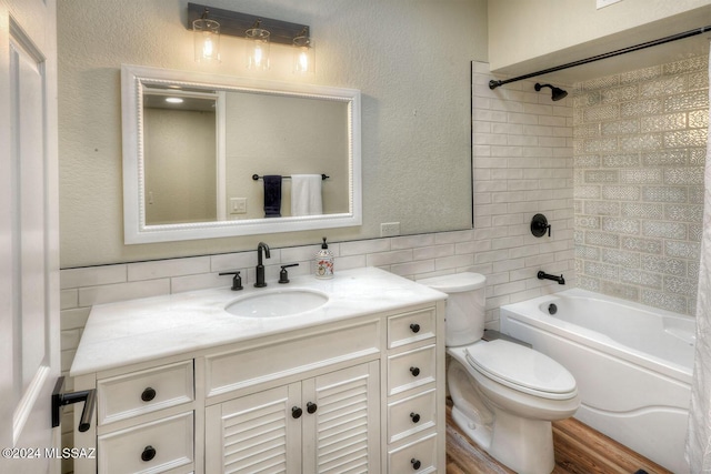 bathroom featuring washtub / shower combination, toilet, vanity, a textured wall, and tile walls