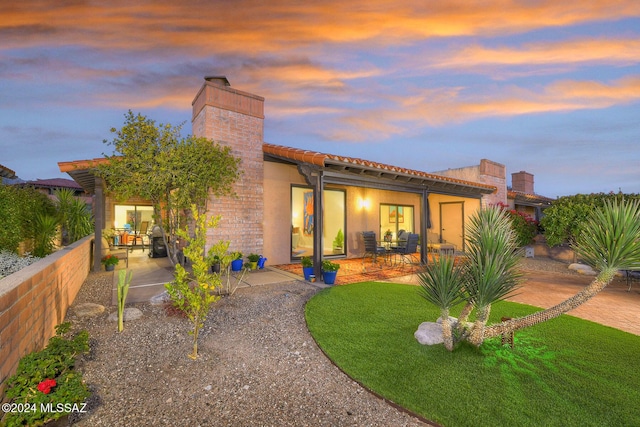 back house at dusk with a yard and a patio area