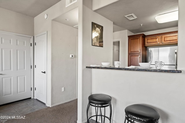 kitchen with dark carpet, a kitchen bar, and stainless steel refrigerator