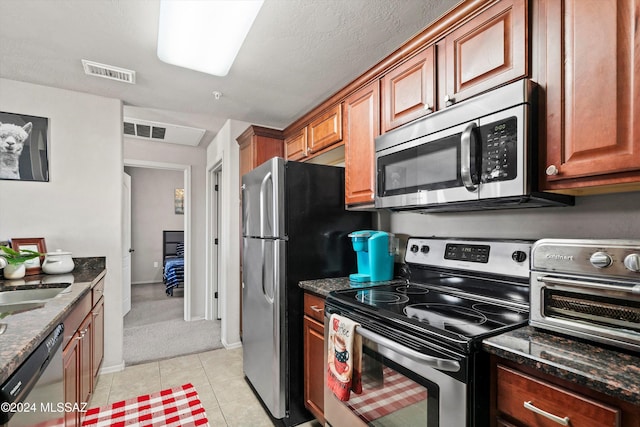 kitchen featuring light tile patterned floors, a textured ceiling, appliances with stainless steel finishes, and dark stone counters