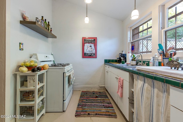 kitchen featuring gas range gas stove, sink, hanging light fixtures, lofted ceiling, and white cabinets