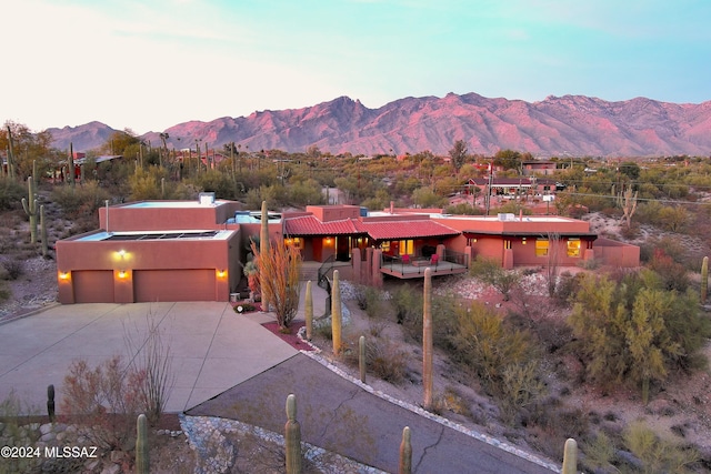 pueblo revival-style home featuring a garage, driveway, a chimney, a mountain view, and stucco siding